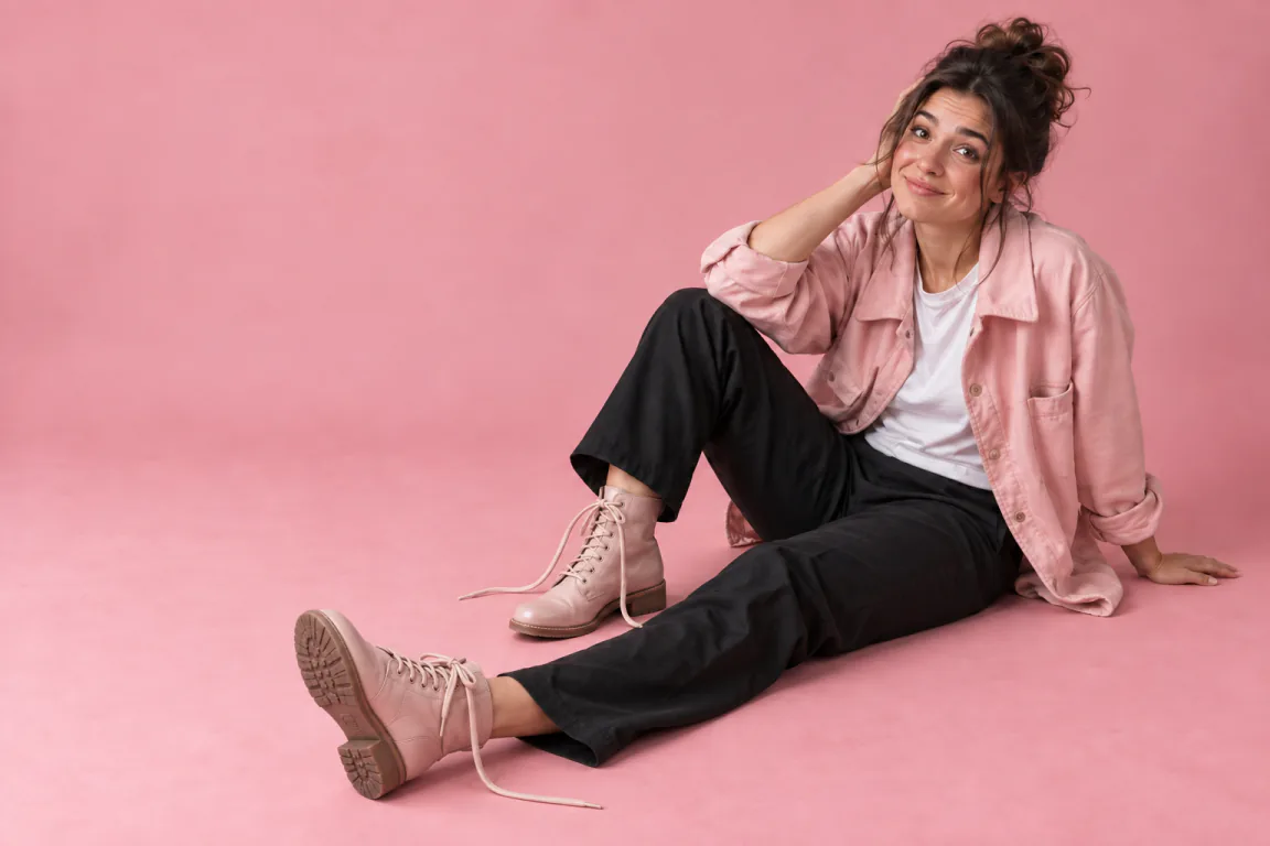 A woman sitting on the studio floor with a sheepish smile after a harmless trip, her pink boots still unlaced